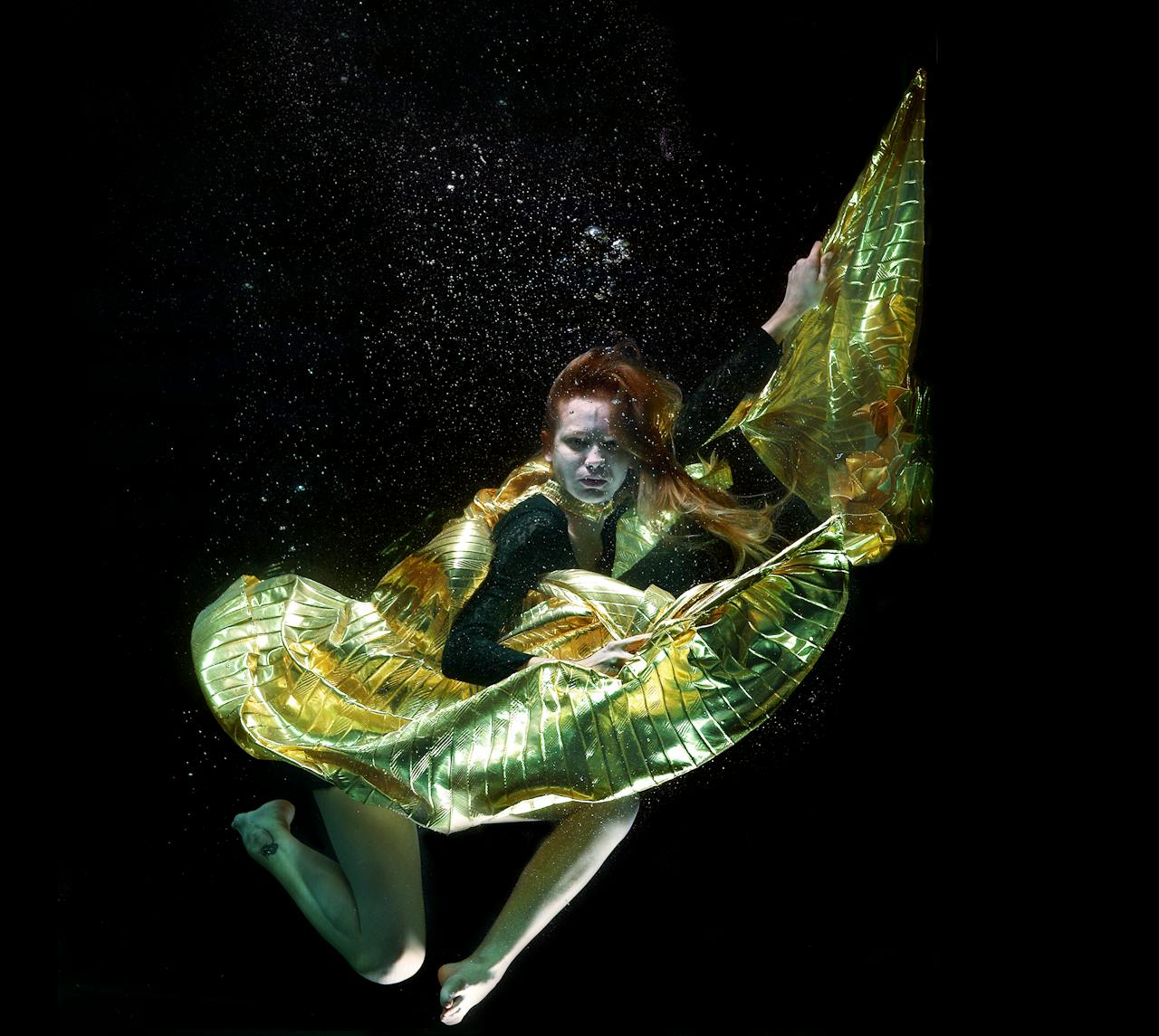 services-01 A woman gracefully dances underwater with shimmering golden fabric, creating an ethereal and fantasy-like scene.